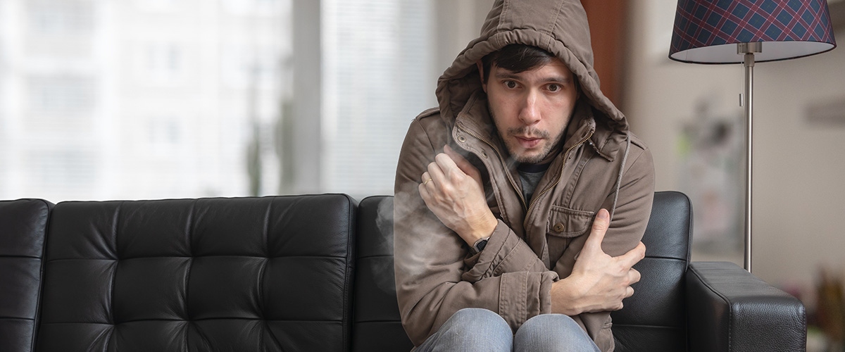 man in coat sitting on sofa shivering from the cold