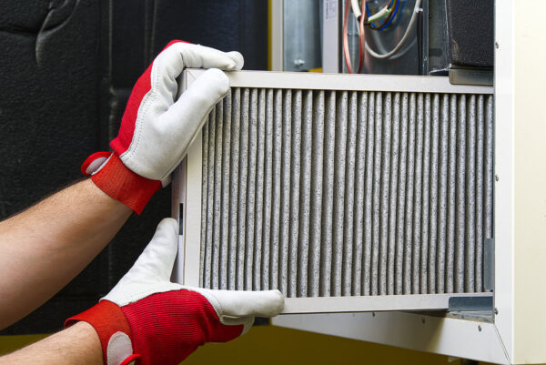 A technician wearing red and white gloves is replacing an air filter in an HVAC unit. This image illustrates the maintenance of an air filtration system to ensure proper indoor air quality.