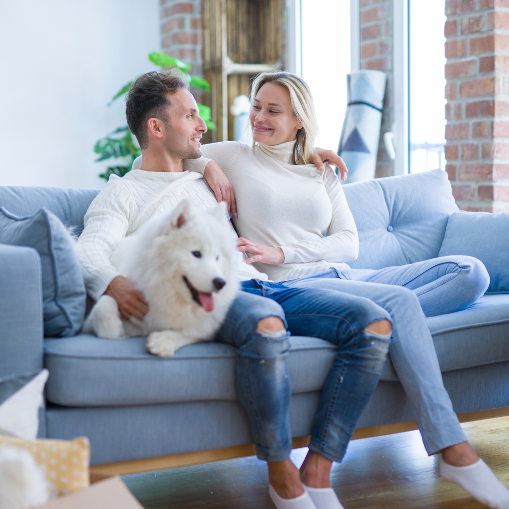 Young beautiful couple with dog sitting on the sofa at new hom