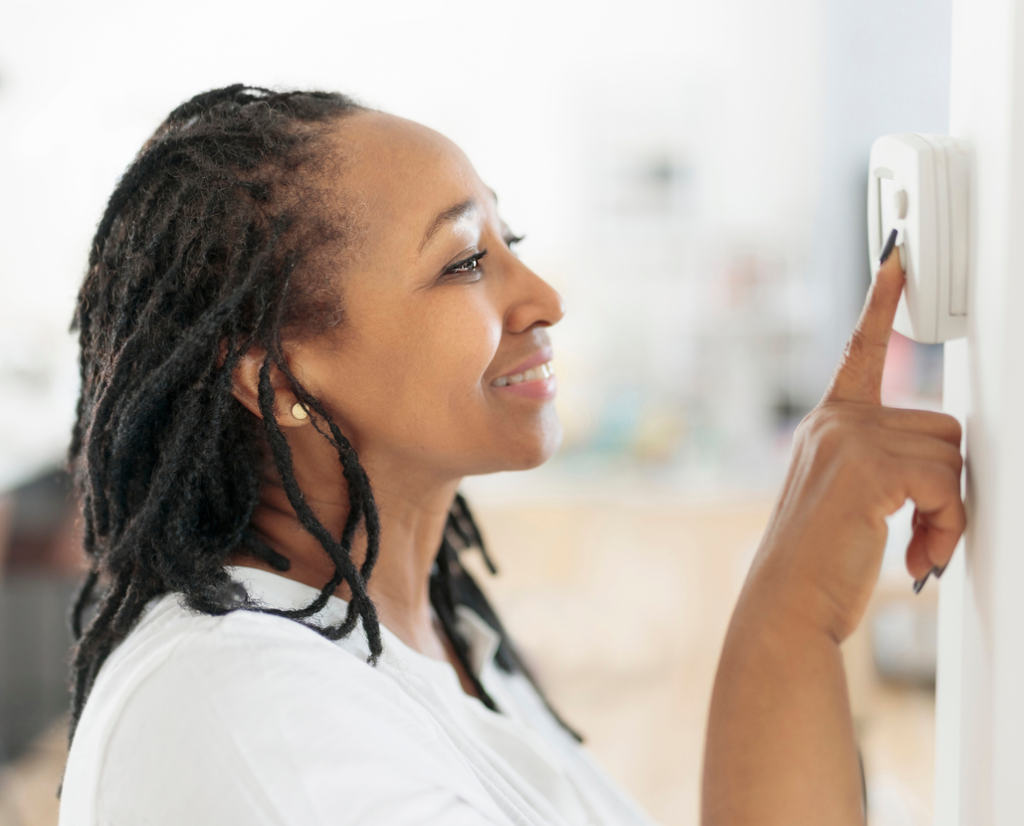 African woman lady adjusting the climate control panel on the wall wall thermostat stock photo