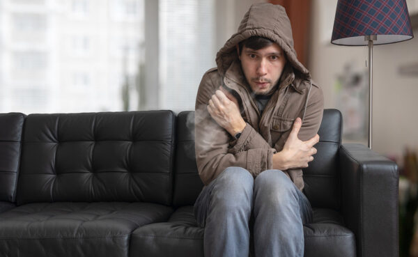 man in coat shivering from cold in his living room