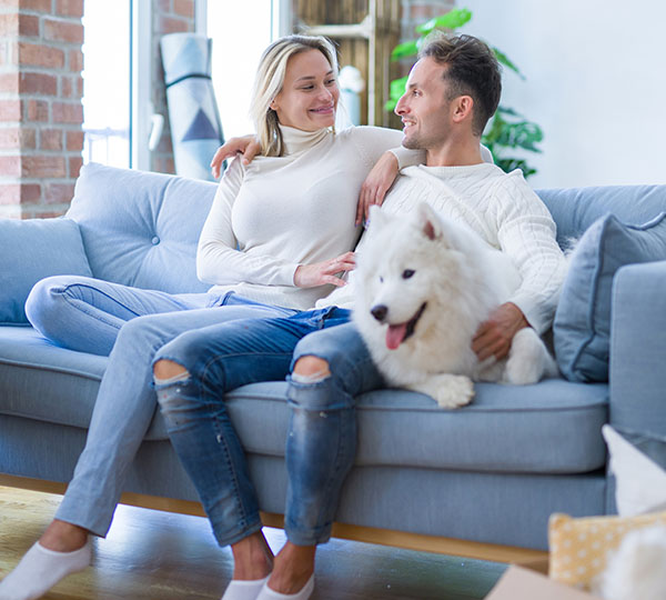Young couple with dog sitting on the sofa at home enjoying purified air