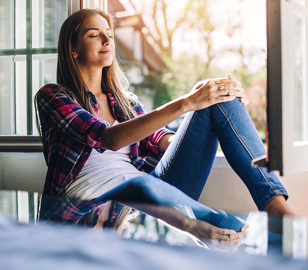 Young woman sitting at a windowsill having rest and fresh air