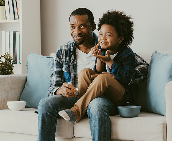 Dad and son sitting on a couch eating snacks enjoying comfortable living